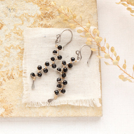 The black tourmaline wrapped mixed metal vine earrings styled on limestone with linen and dried grass
