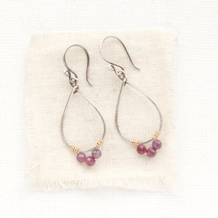 The purple ruby wrapped teardrop hoop earrings styled on tan linen