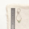 A green apatite wrapped teardrop hoop earring next to a ruler for size reference