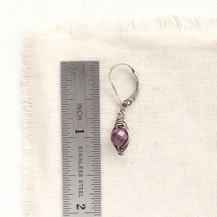 A perfect wrap purple ruby earring next to a ruler for size reference