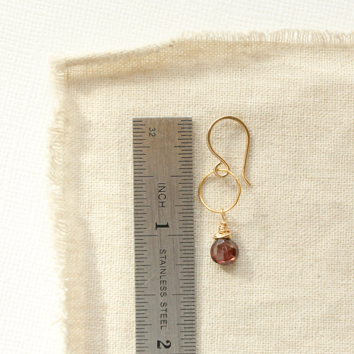 A garnet gold hoop earring next to a ruler for size reference