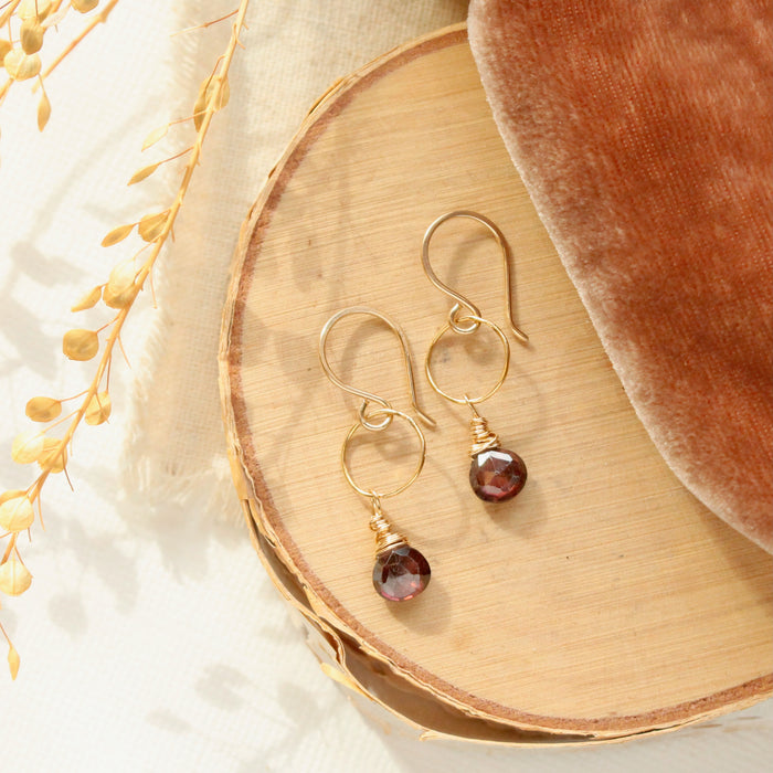 The garnet drop gold hoop earrings style on wood with velvet and dried grass.