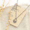 The mini talara shield necklace styled on a tan rock with linen and dried grass