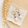 The pearl and ruby gold earrings styled on a tan plate with linen and dried grass