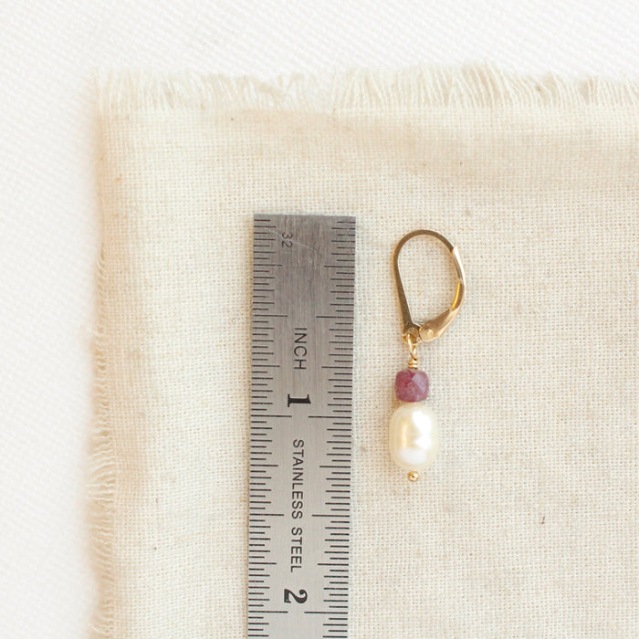 A pearl and ruby gold earring next to a ruler for size reference
