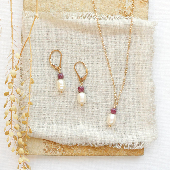 The pearl and ruby gold earrings styled on a tan rock with the matching necklace
