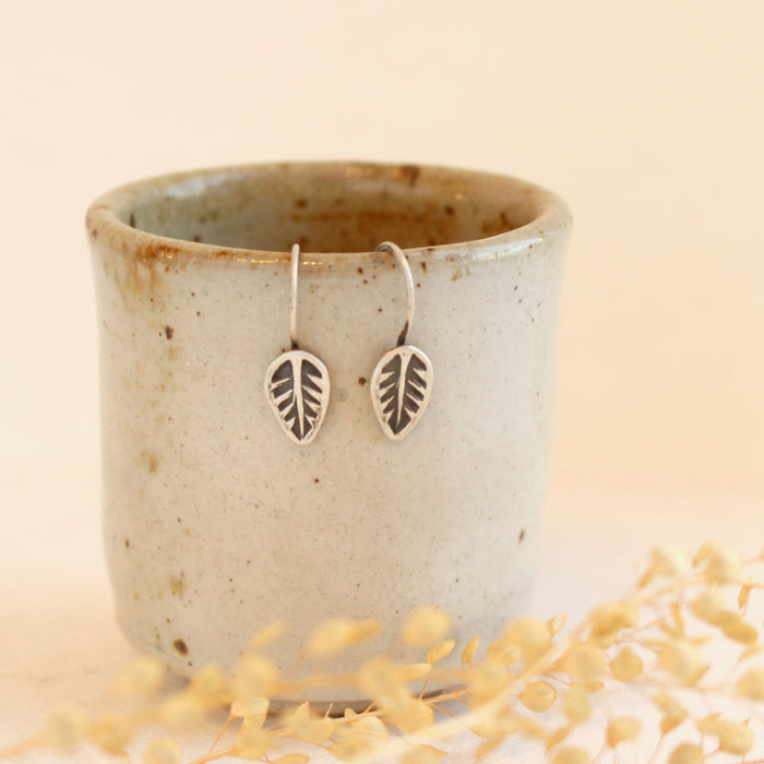 the little leaf lobe hugger earrings styled on a ceramic cup with dried grass