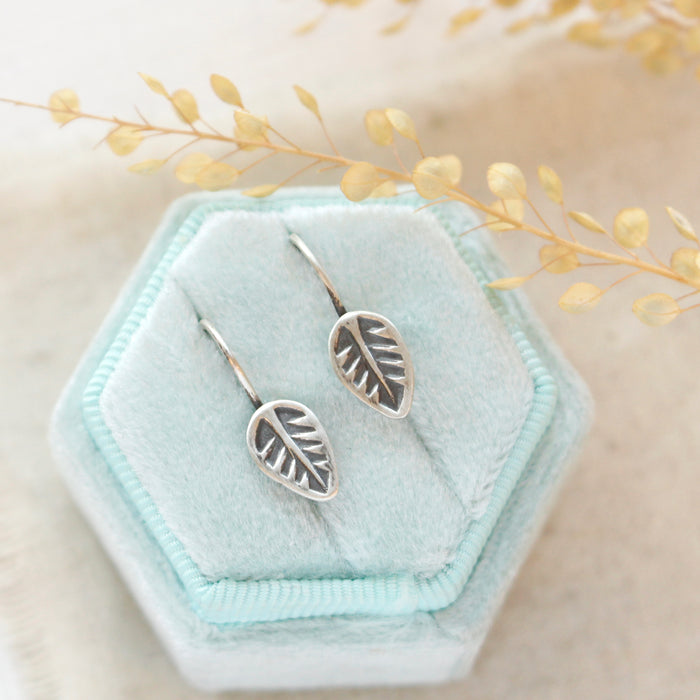 The little leaf lobe hugger earrings styled on a blue velvet box with linen and dried grass