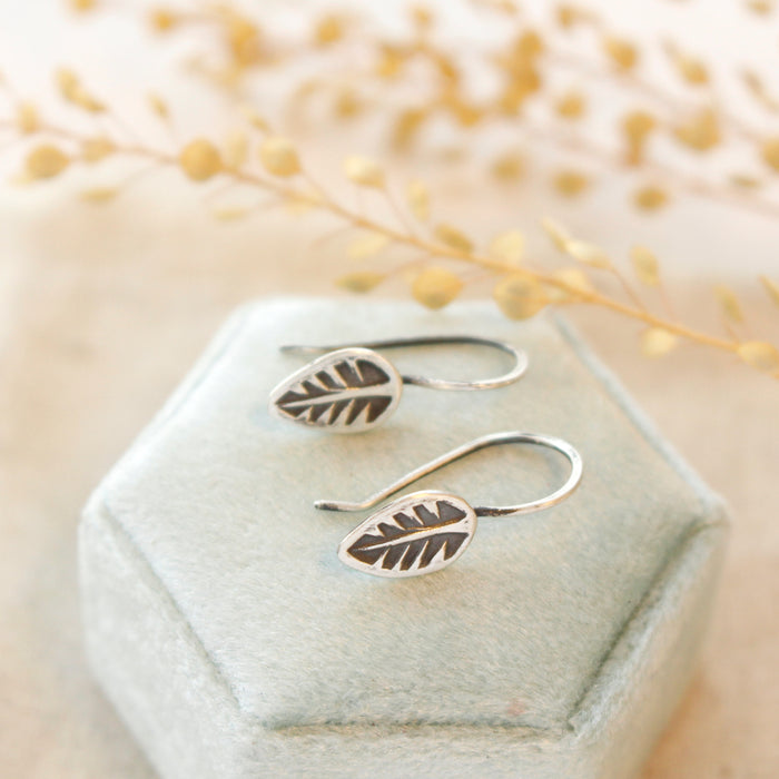 The little leaf lobe hugger earrings styled on a blue velvet box with dried grass