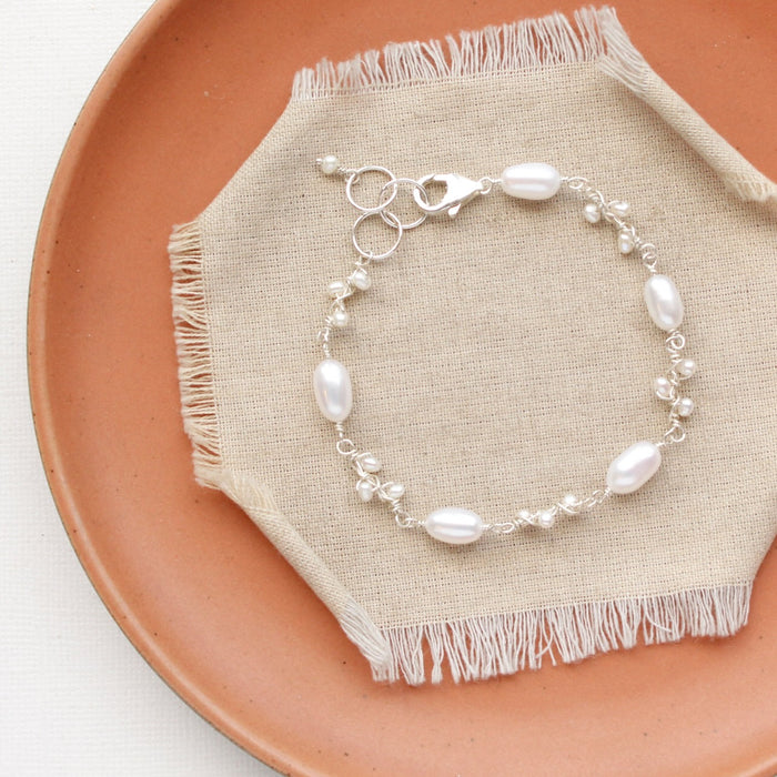 The bright silver wrapped pearl bud vine bracelet styled on an orange plate with linen