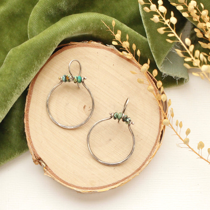 The african jasper halo hoop earrings styled on wood with green velvet and dried grass