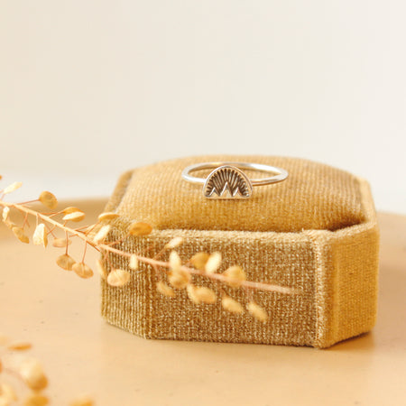 The alpine glow stacking ring styled on a yellow velvet box with dried grass