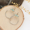 The amazonite halo hoop earring styled on wood with gray velvet and dried grass