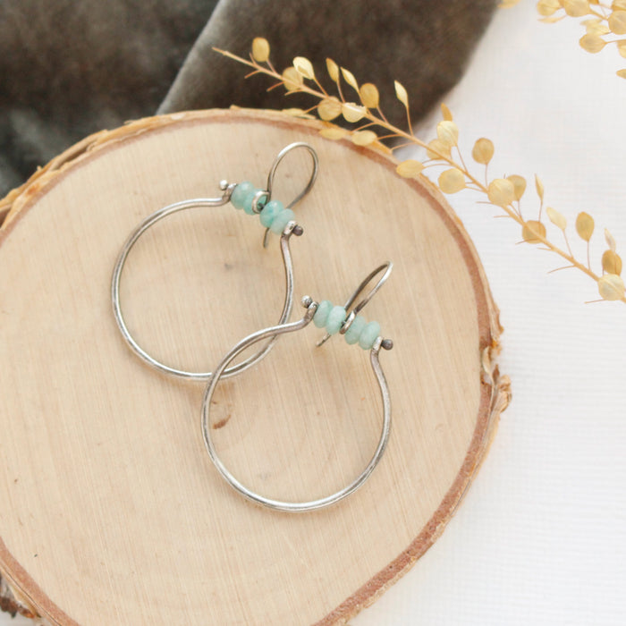 The amazonite halo hoop earring styled on wood with gray velvet and dried grass