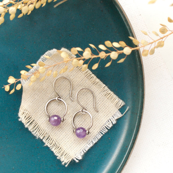 The amethyst la cloche earrings styled on a blue plate with linen and dried grass