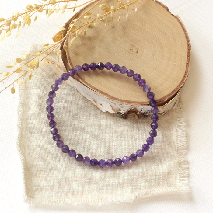 The amethyst stretch bracelet styled on wood with linen and dried grass