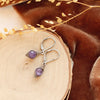 The wrapped amethyst earrings styled on wood with orange velvet and dried grass