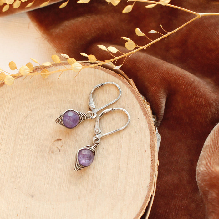 The wrapped amethyst earrings styled on wood with orange velvet and dried grass