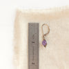 A wrapped amethyst earring next to a ruler for size reference