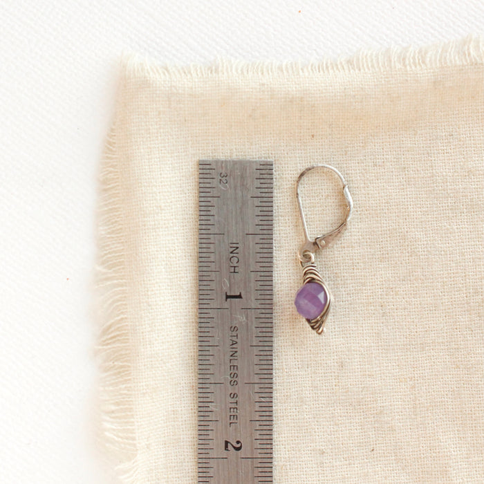 A wrapped amethyst earring next to a ruler for size reference