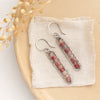 The andesine beaded bar earrings styled on a tan plate with linen and dried grass