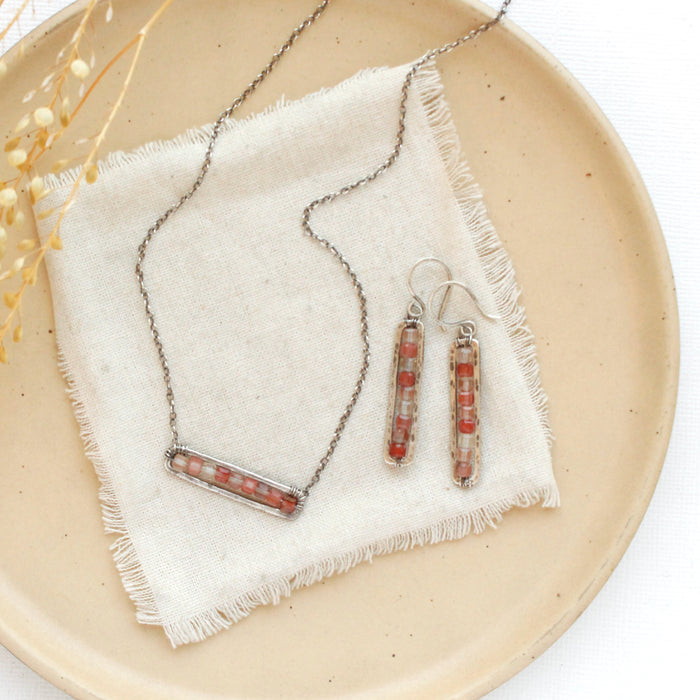 The andesine beaded bar earrings styled with the matching necklace on a tan plate with linen and dried grass