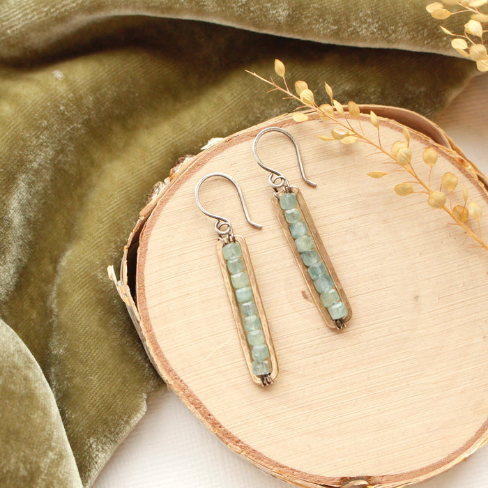 The apatite beaded bronze bar earrings styled on wood with green velvet and dried grass
