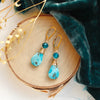 The apatite and turquoise drop earrings styled on wood with blue velvet and dried grass