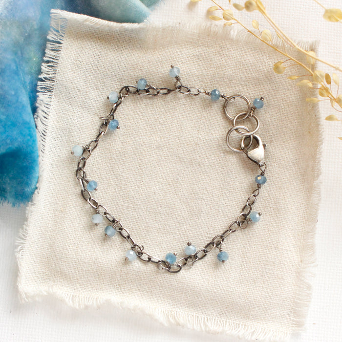 The aquamarine charm bracelet styled on tan linen with blue velvet and dried grass