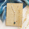 The aquamarine drop lariat necklace styled on a tan rock with blue velvet and dried grass