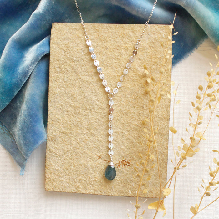 The aquamarine drop lariat necklace styled on a tan rock with blue velvet and dried grass