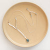 The aquamarine drop lariat necklace styled on a tan plate to show the adjustable lobster clasp closure
