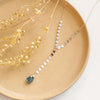 The aquamarine drop lariat necklace styled on a tan plate with dried grass