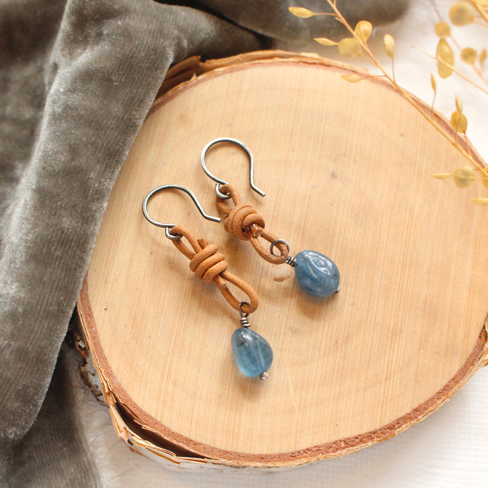 The aquamarine leather earrings styled on wood with gray velvet and dried grass