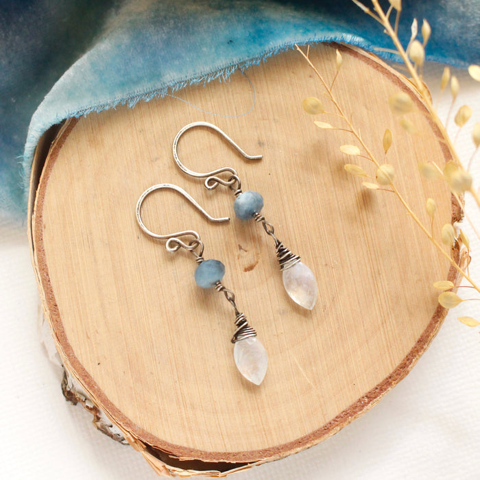 The aquamarine and moonstone earrings styled on wood with blue velvet and dried grass