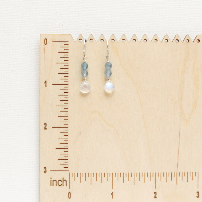 The aquamarine and moonstone earrings styled on a wooden ruler for size reference