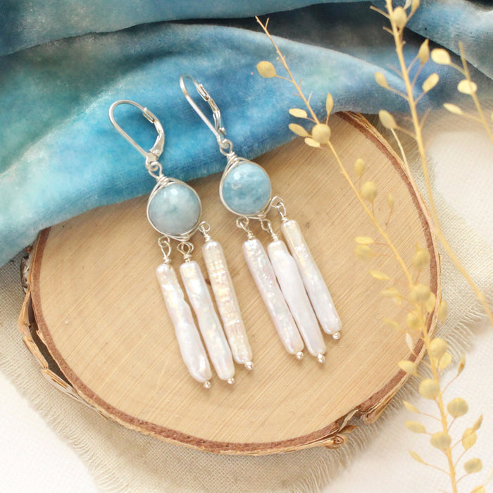 The aquamarine and pearl chandelier earrings styled on wood with blue velvet and dried grass