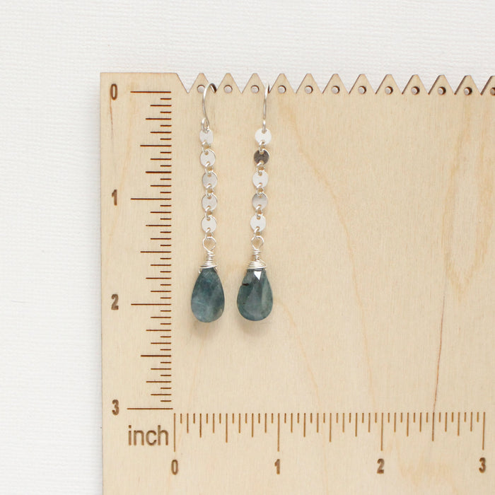 The aquamarine and disc chain earrings styled on a wooden ruler