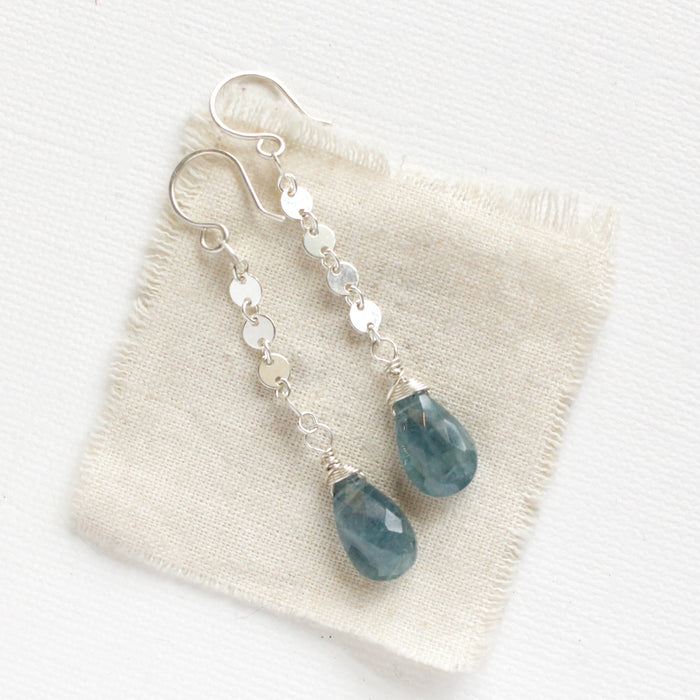 The aquamarine drop and silver disc long earrings styled on tan linen