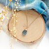 The aquamarine drop necklace styled on wood with blue velvet and dried grass
