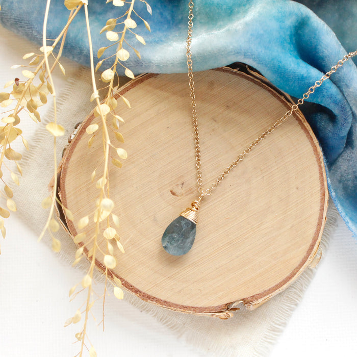 The aquamarine drop necklace styled on wood with blue velvet and dried grass