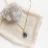 The aquamarine drop necklace styled on tan linen with a gray crystal