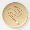The baroque pearl necklace styled on a tan plate to show the adjustable lobster clasp closure