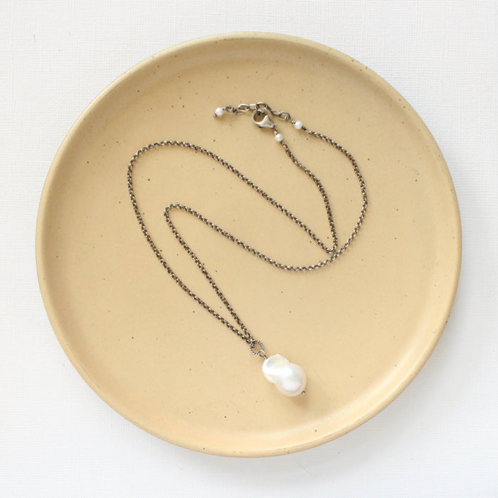 The baroque pearl necklace styled on a tan plate to show the adjustable lobster clasp closure