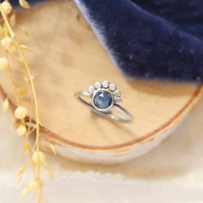 The beaded sapphire ring styled on wood with blue velvet and dried grass