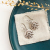 The big musana earrings styled on a blue plate with linen and dried grass
