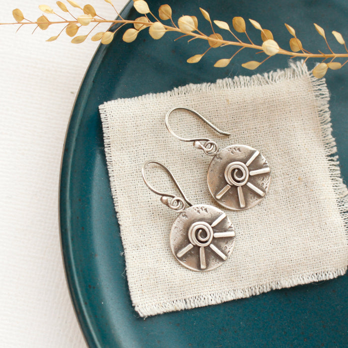 The big musana earrings styled on a blue plate with linen and dried grass
