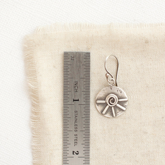 A big musana earring next to a ruler for size reference