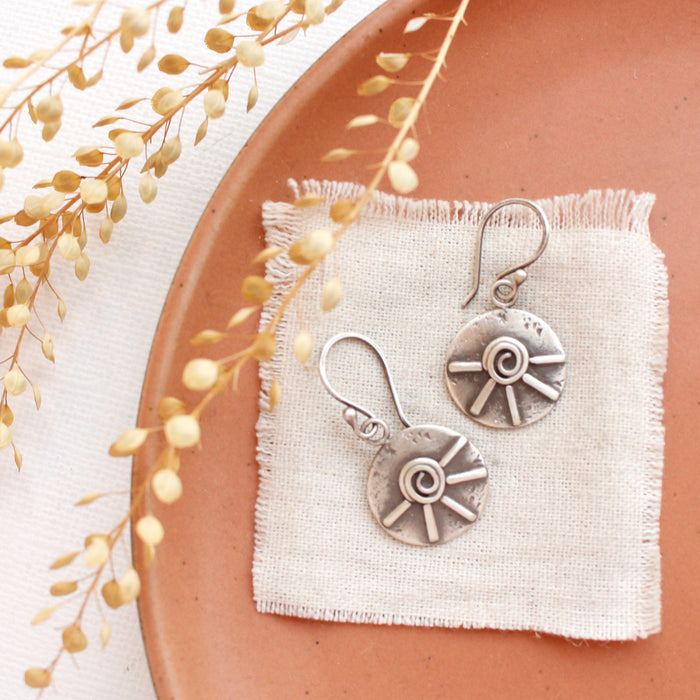 The big musana earrings styled on an orange plate with linen and dried grass
