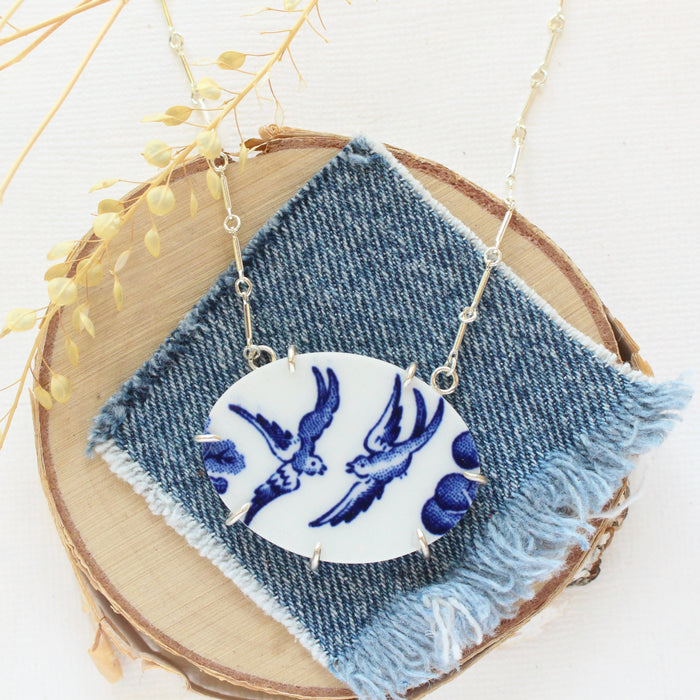 The birds of a feather vintage plate necklace styled on wood with blue linen and dried grass